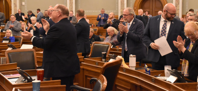 Speaker Dan Hawkins, left, and other members of the Kansas House applaud in the early hours of April 6 after passing a tax cut package.